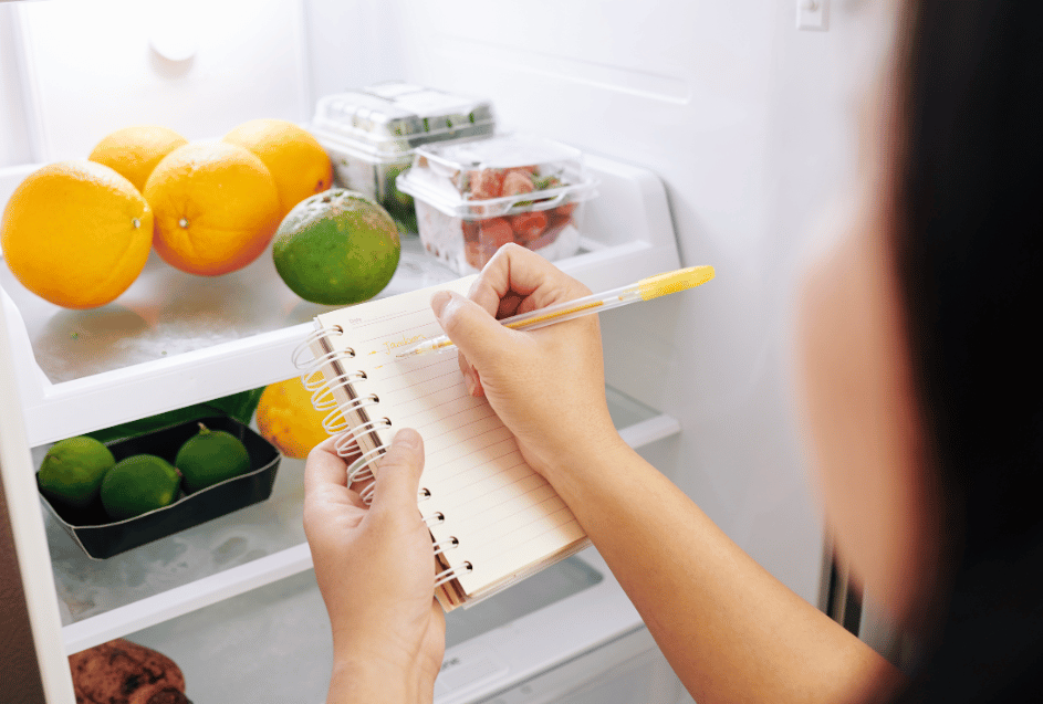 Mulher fazendo lista e conferindo ingredientes na geladeira